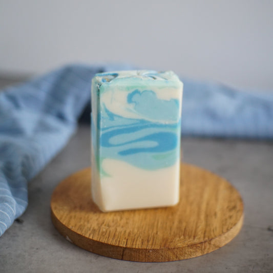A rectangular Sea Salt and Sage Aloe and Shea Soap bar on a round wooden tray.