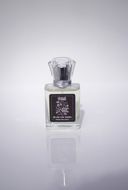 Blush and Thorn Perfume bottle with a label on a white reflective surface
