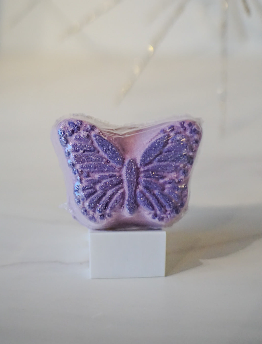 Purple butterfly-shaped bath bomb scented in lavender santal  on a white stand with a white background