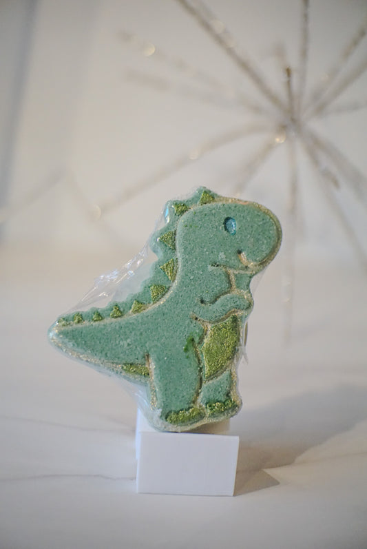 Green dinosaur-shaped bath bomb on a white stand with a white background