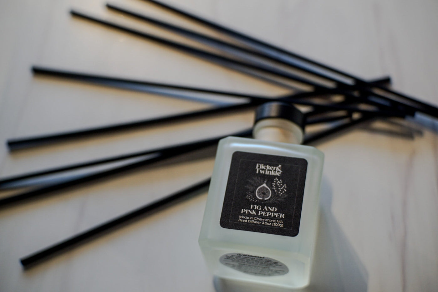 Fig and Pink Pepper Reed diffuser with black label on a light background with black reeds. 