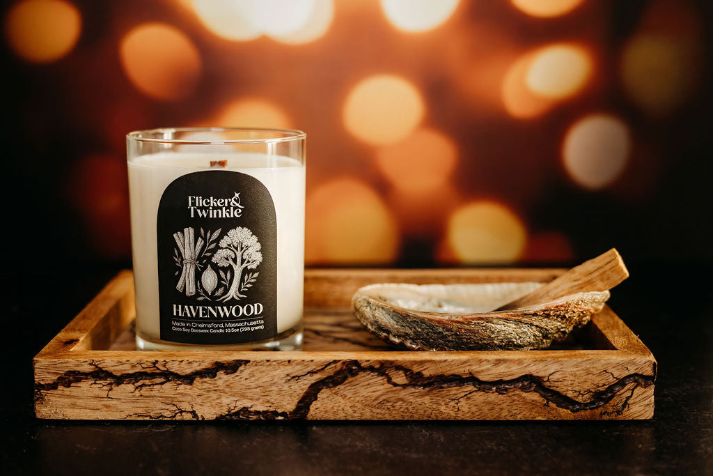 Sandalwood scented Candle labeled 'Flicker & Twinkle Havenwood' on a wooden tray with a blurred warm light background.
