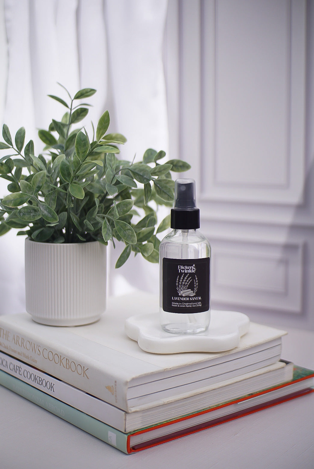Bottle of room and Linen spray on a stack of books with a plant in the background