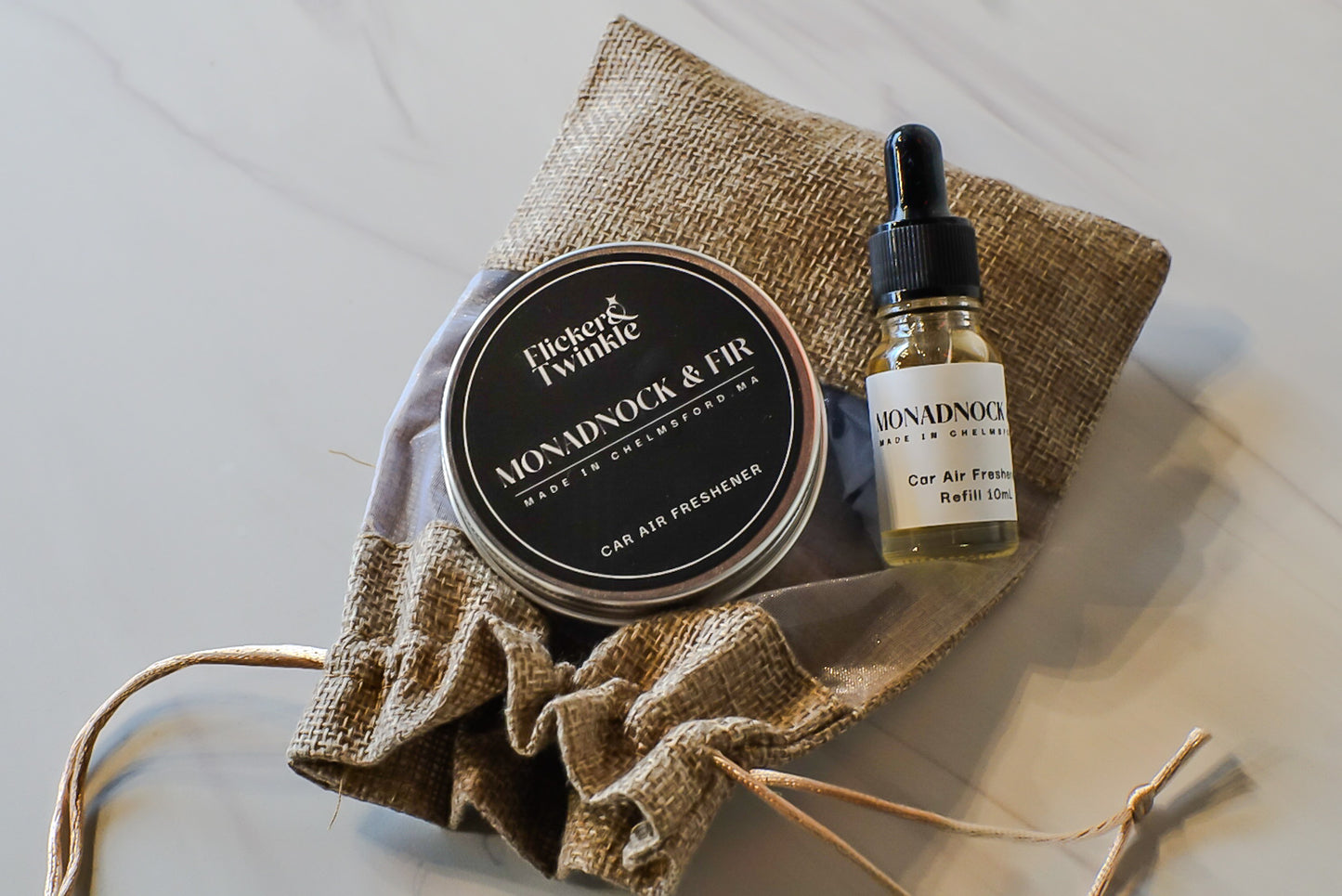 Car air freshener tin and bottle with Monadnock and Fir branding on a textured surface.