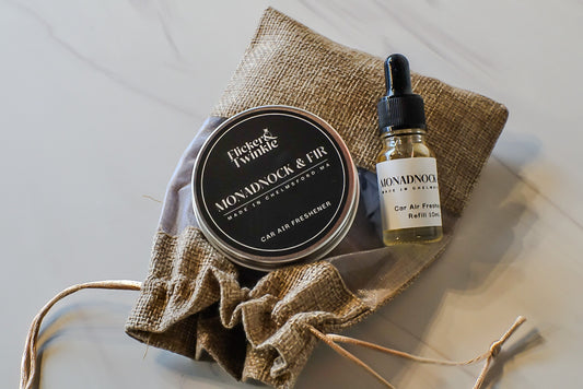 Car air freshener tin and bottle with Monadnock and Fir branding on a textured surface.