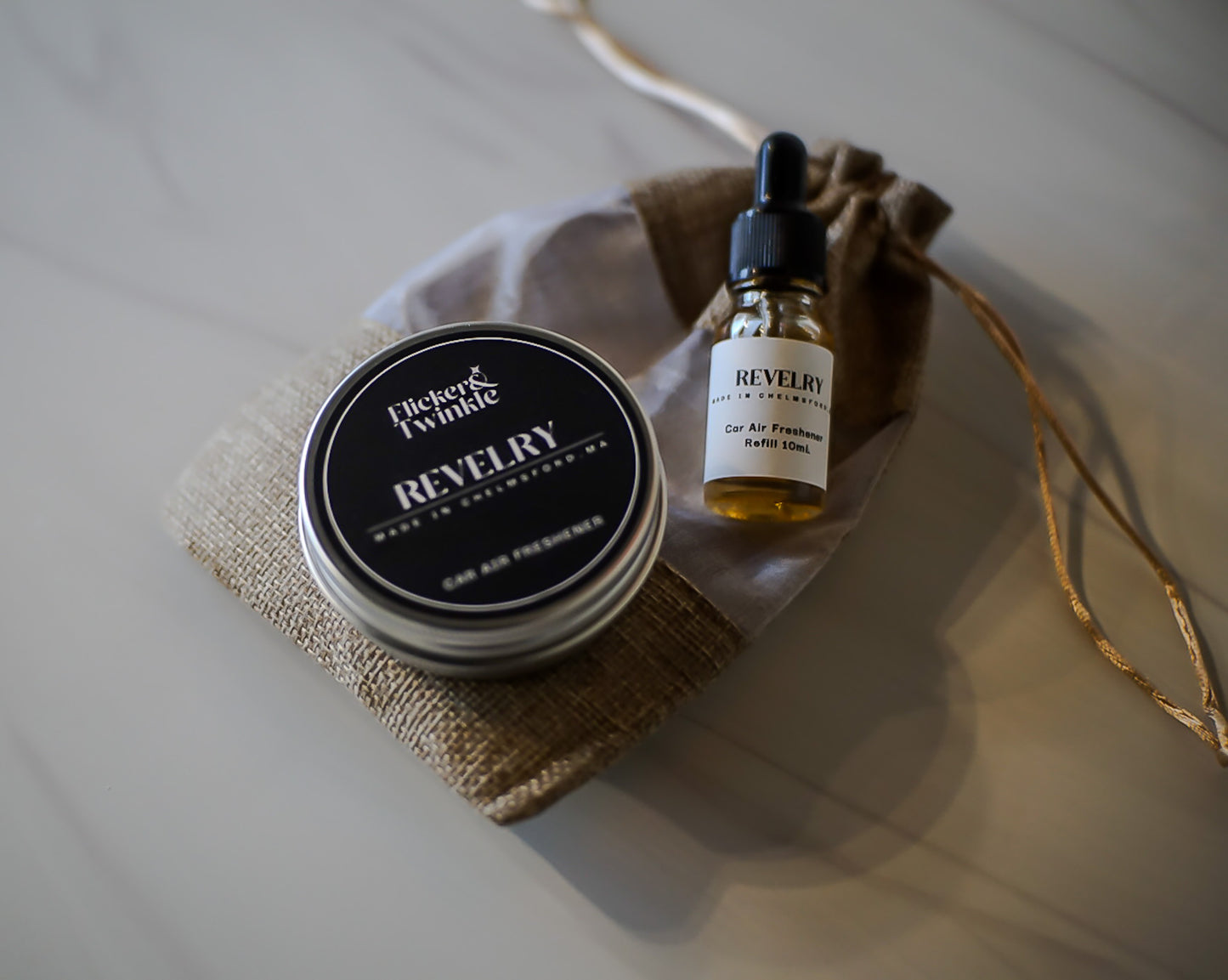 Car Freshenr tin and dropper bottle with 'Revelry' scent on a textured surface