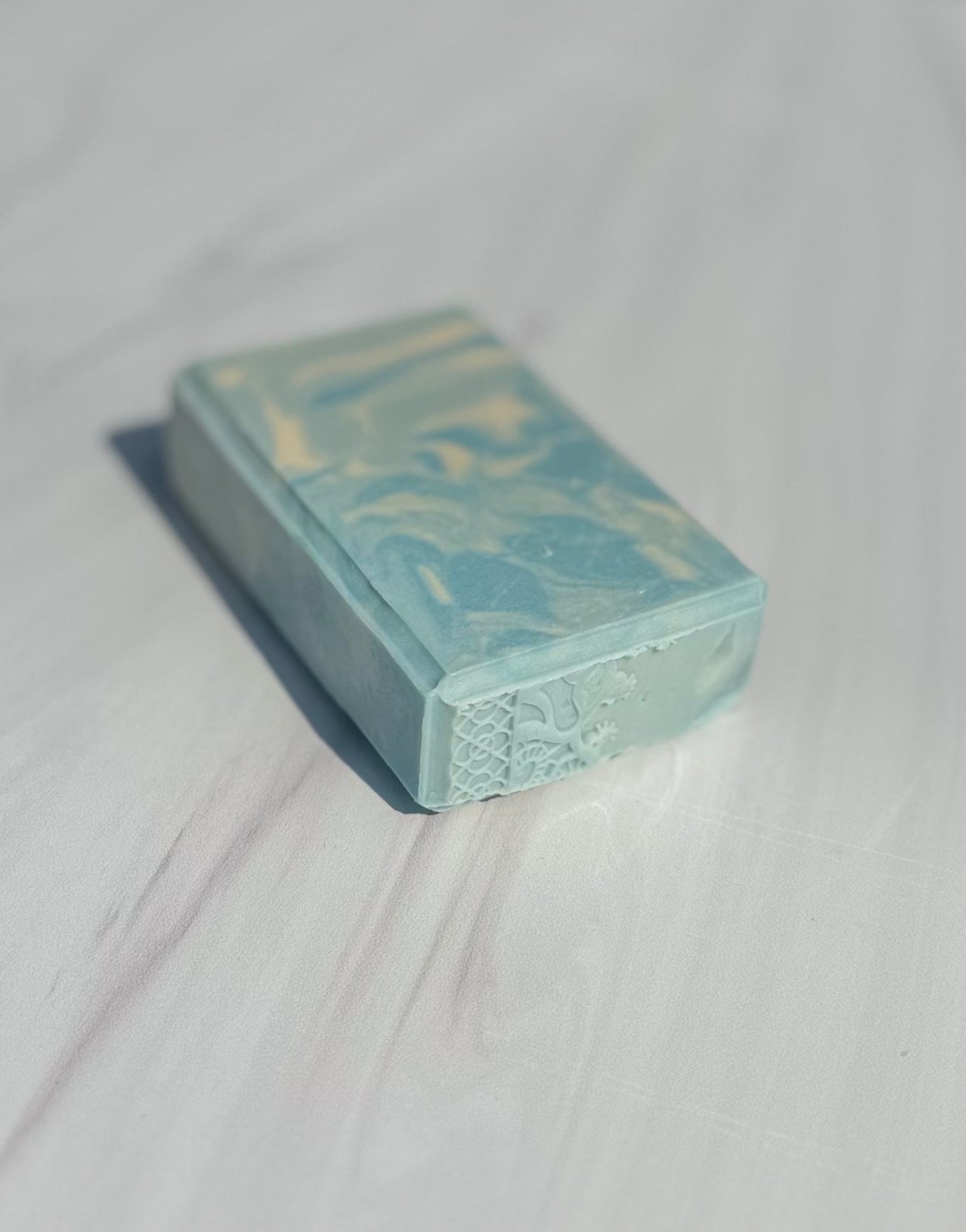 A rectangular bar of soap scented with "The Naiad" with a light blue and white marbled pattern, resting on a white marble surface.
