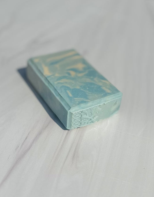 A rectangular bar of soap scented with "The Naiad" with a light blue and white marbled pattern, resting on a white marble surface.