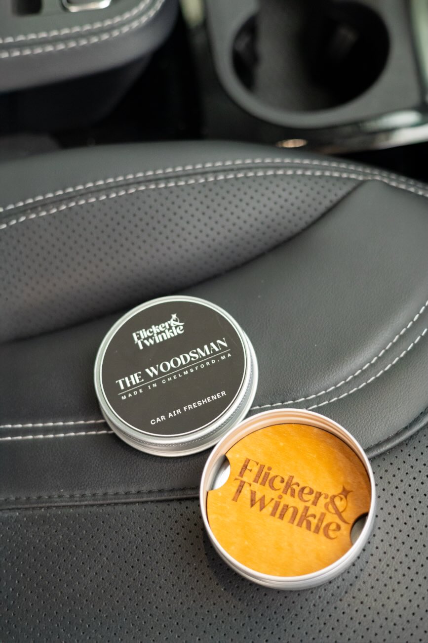 The Woodsman refillable car air freshener in car—open wood diffuser tin with 10 mL refill bottle.
