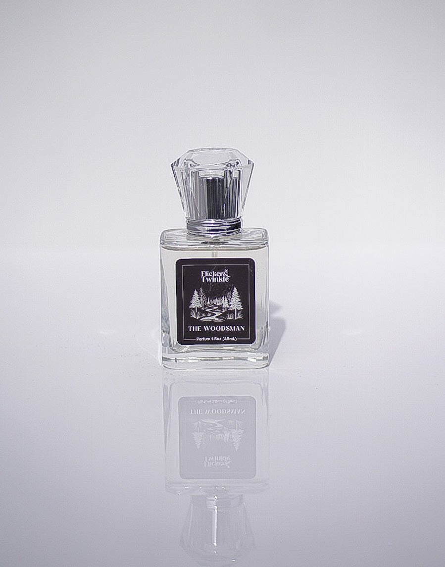 A clear glass bottle of The Woodsman Parfum on a white background with reflection.