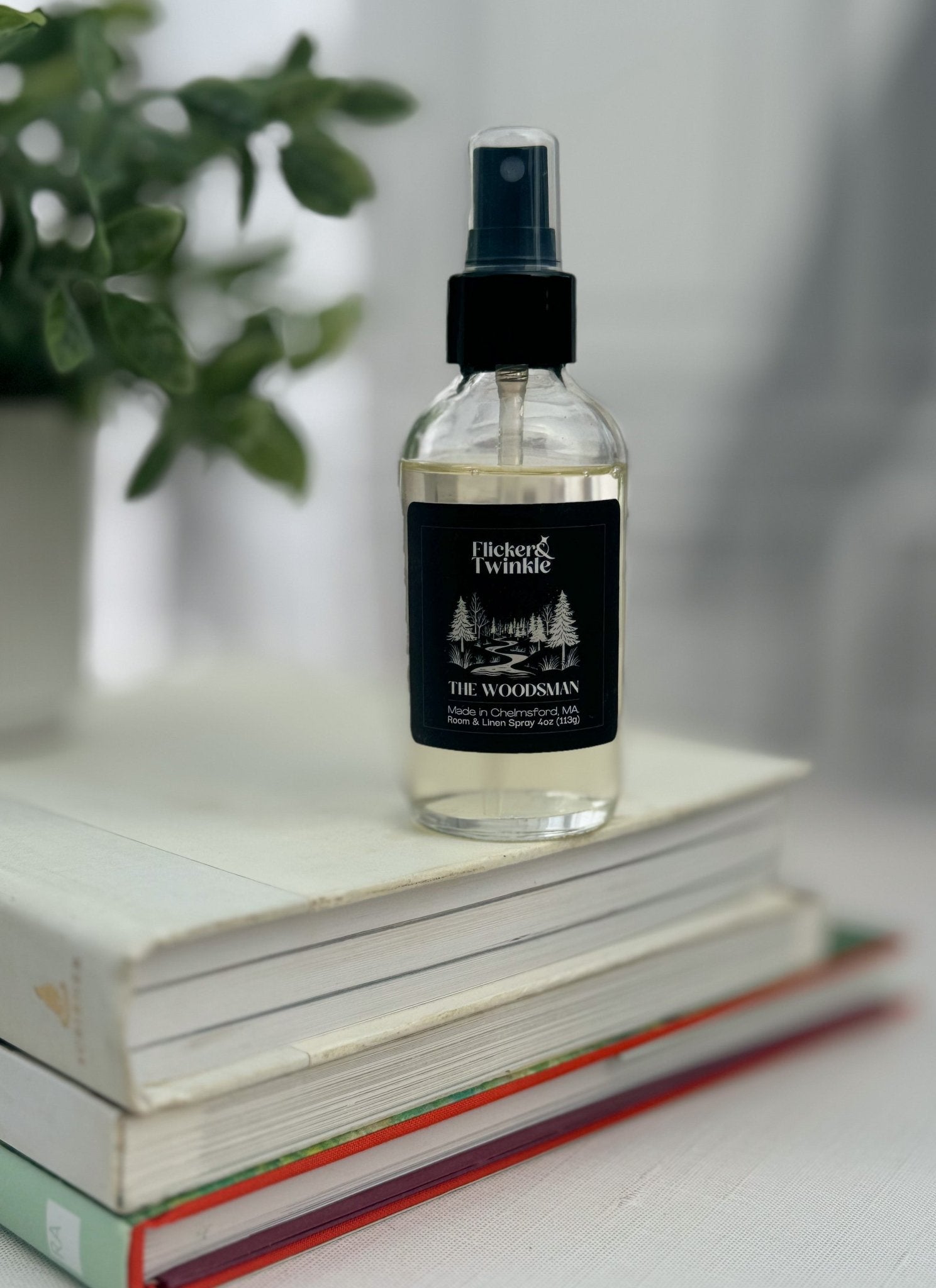 The Woodsman Room and Linen Spray rests atop books beside a potted plant.