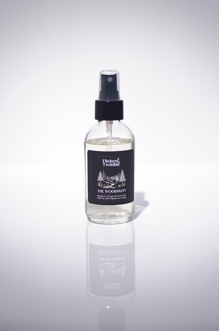 A clear spray bottle labeled The Woodsman Room and Linen Spray with black and white branding.