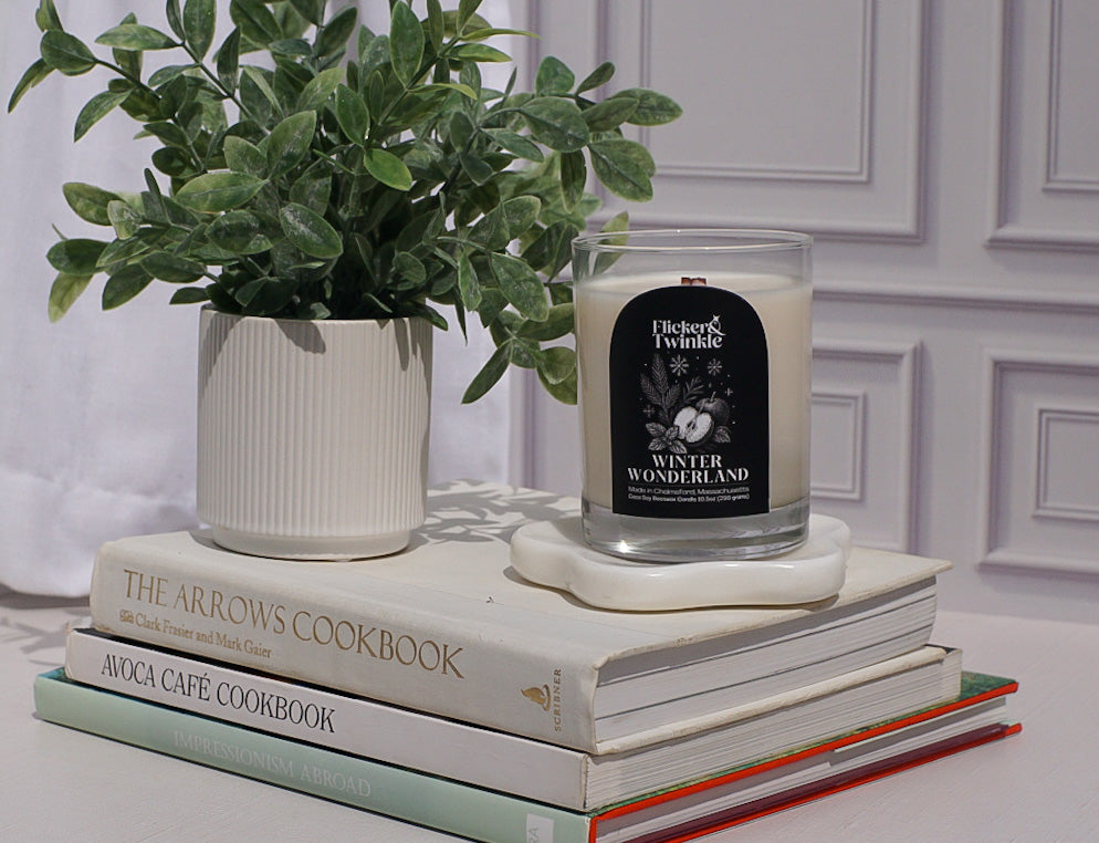 Candle on a stack of books with a plant next to it against a white wall.