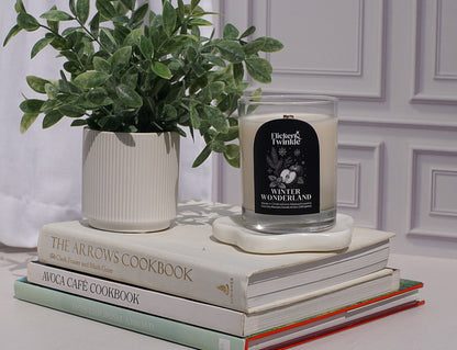Candle on a stack of books with a plant next to it against a white wall.