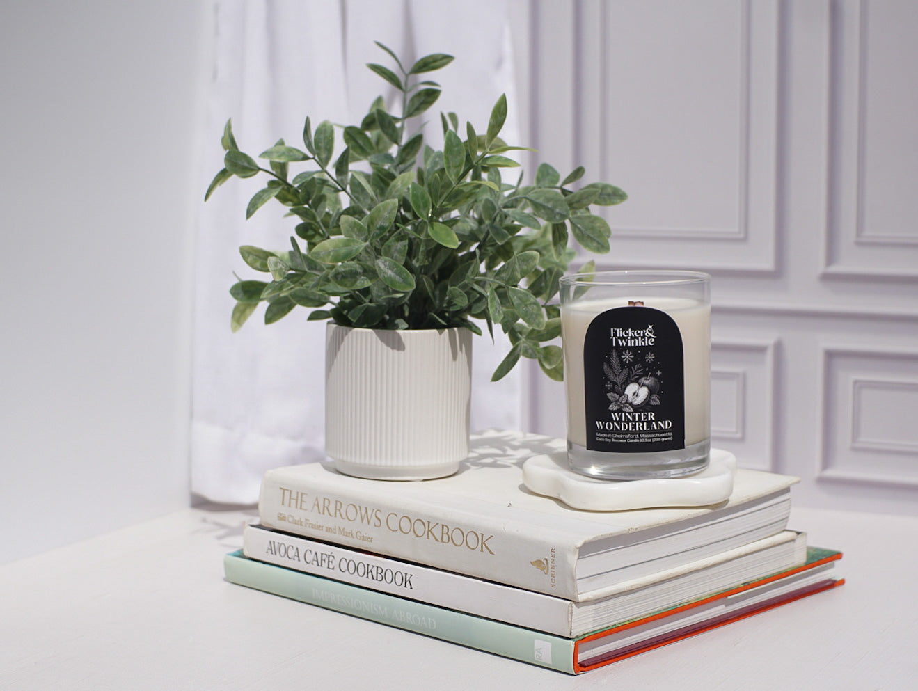 Stack of cookbooks with a candle and plant on a white surface