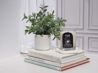 Stack of cookbooks with a candle and plant on a white surface