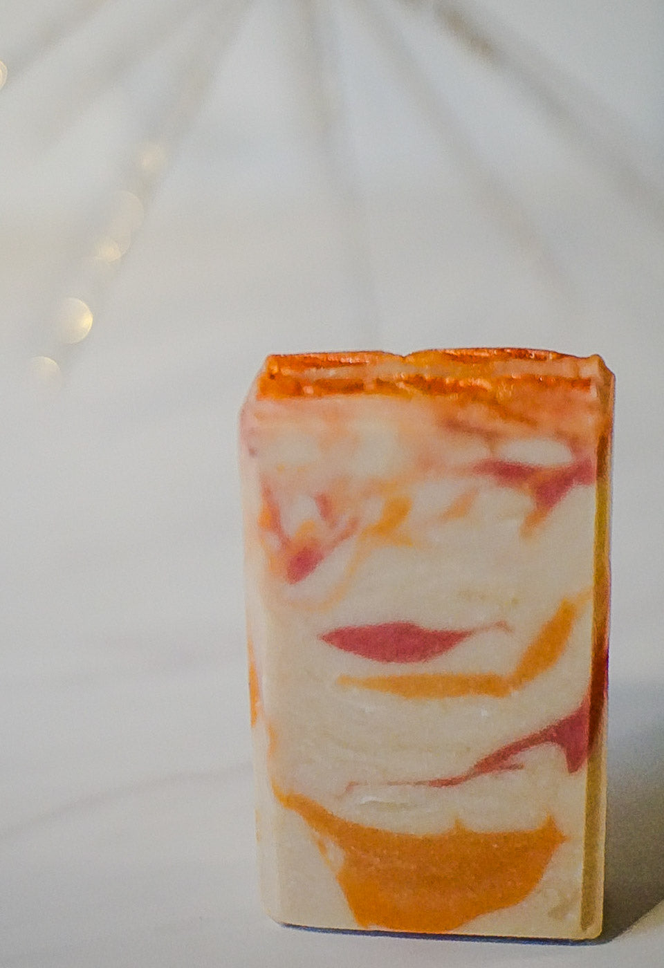 Marbled orange and cranberry goat milk soap bar with orange and white colors on a white background
